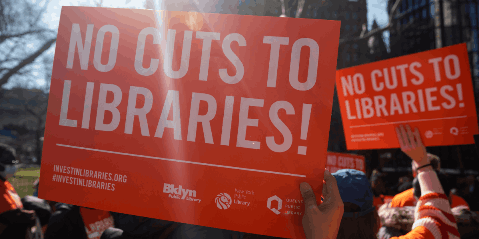 close up of sign held up at outdoor rally that reads: No Cuts to Libraries!