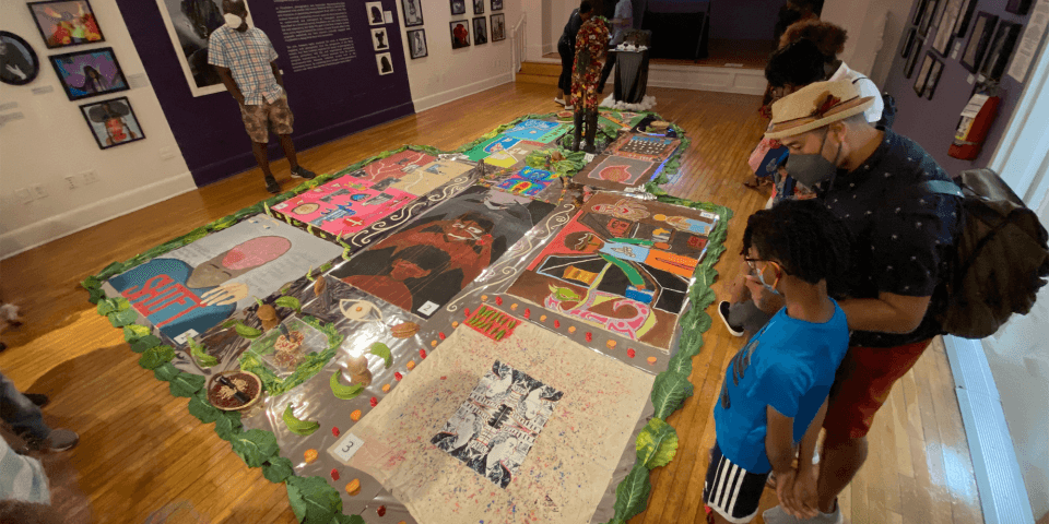 A group of people looking at the paintings and sculptures, which are placed on the floor.