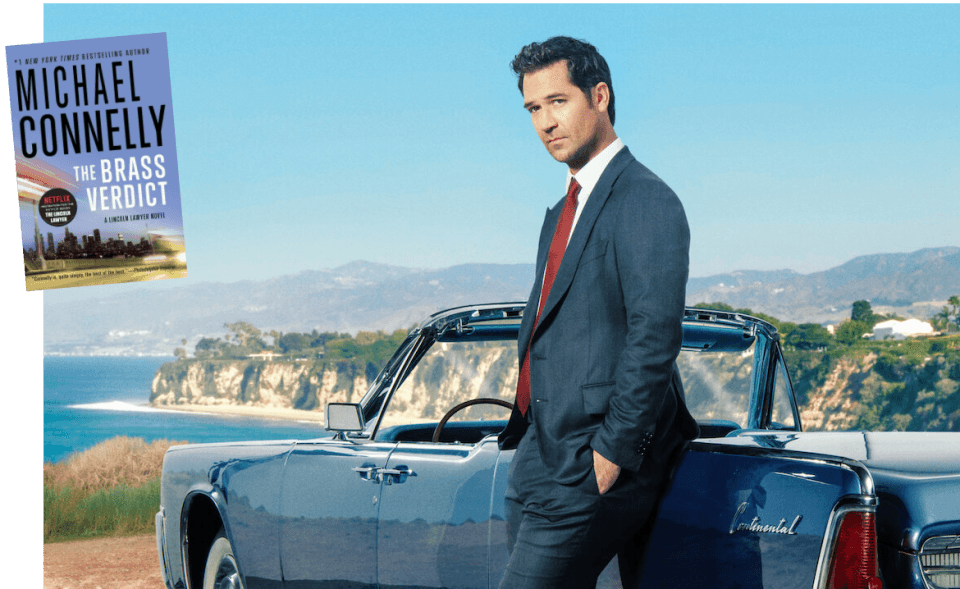 man in a suit leaning against a convertible car parked overlooking the ocean