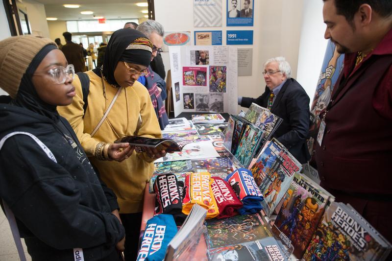A group of people standig around a table and reading comic books.