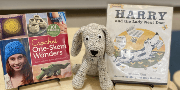 crocheted dog with a picture book and an instructional crochet book