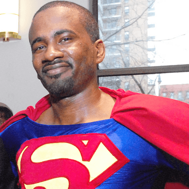 Cosplayer Michael Flood dressed as Superman. He is wearing a red cap, blue shirt with an letter 