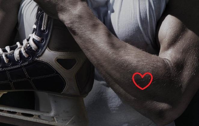 A flexed man's arm holds a hockey skate, with an illustration of a heart on the arm