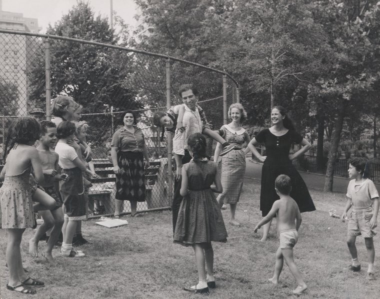 kids gathered outside monkeying around with a man while two women stand nearby