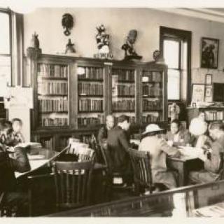 Black and white image of people studying in library room.