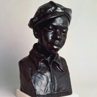 A bust of a young Black man wearing a newsboy style cap. It was created by Augusta Savage in 1929.
