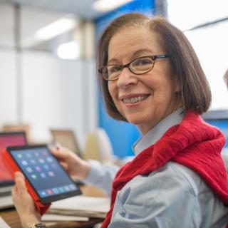 A library patron is holding an iPad and smiling at the camera.