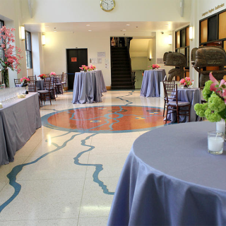 Circle-shaped tables covered with blue tablecloths and chairs are arranged in the Langston Hughes Lobby. Along the left side is a rectuangular shaped table that has glasses on top. It is covered with a blue table cloth.