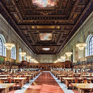 The Rose Main Reading Room on a sunny day with a walkway dividing the room into two sections populated with long desks, chandeliers, domed windows, and a cloud-filled mural mounted on an ornate ceiling.