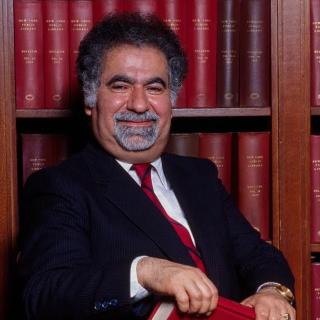 Portrait of Vartan Gregorian wearing a suit, seated in front of a shelf lined with red books.