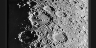 Black-and-white transparency showing a close-up of a portion of the moons cratered surface, its horizon curving in the upper right corner of the image