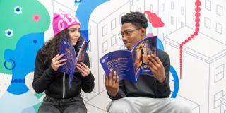Two teens reading 'Teen Voices' magazine in front of a colorful wall mural.