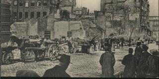 Black and white postcard showing destruction of buildings with people looking at scene in foreground