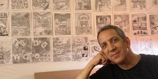 Peter Kuper sits in front of his drawings pinned to the wall