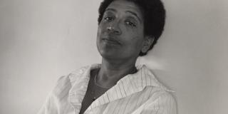 Black and white photograph portrait of the author Audre Lorde; she faces the camera, wears light colored blouse