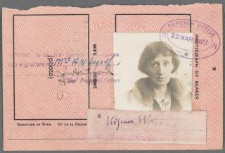 A pink passport page with a torn ragged edge shows a black-and-white photograph of a woman with short hair wearing a coat with a fur collar, a slip of paper signed "Virginia Woolf," and a stamp reading "Foreign Office, 22 Mar 1923." 