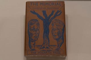 Book cover of The Memorial by Christopher Isherwood published by the Hogarth Press, with a blue drawing of a tree between two large faces and blue text