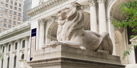 Marble lion statue in front of the Stephen A. Schwarzman Building, which is displaying a Treasures-themed banner in the background.