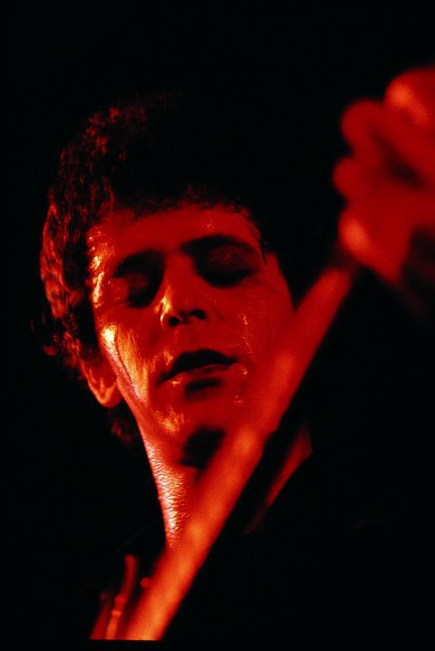 A black and red photo of Lou Reed face, eyes closed, holding the neck of his guitar.