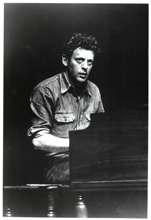 A black and white photo of a man behind a piano.