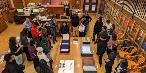 Bird's eye view of a class attending a lecture around a table filled with historic books. 