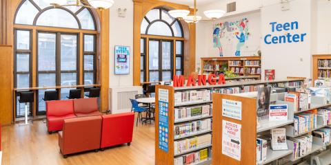 Teen Center at Chatham Square Library, featuring rows of bookshelves, red reading chairs, and large arched windows.